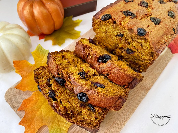 Slices of pumpkin cranberry bread on wooden board with fall decor